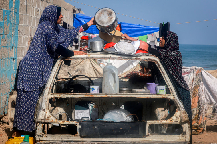 نساء فلسطينيات يرتبن أدوات المطبخ لتجفيفها فوق سيارة مدمرة في مخيم مؤقت للنازحين.