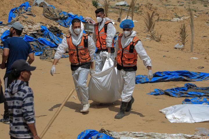 عمال يحملون جثة عثر عليها في مقبرة جماعية في مستشفى ناصر بمدينة خان يونس جنوب قطاع غزة.