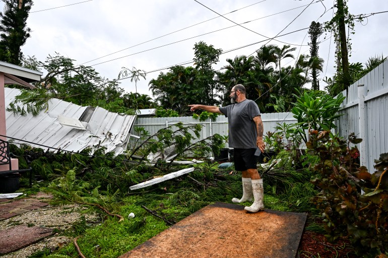 Dan Jones points toward a destroyed roof in his backyard after a tornado hit in Fort Myers, Florida on October 9, 2024, as Hurricane Milton approaches. - Many Florida residents have fled, but some battened down the hatches, in the final hours October 9, 2024 before Hurricane Milton pummels the state, as government relief efforts were dragged into the thick of the White House race. (Photo by CHANDAN KHANNA / AFP)